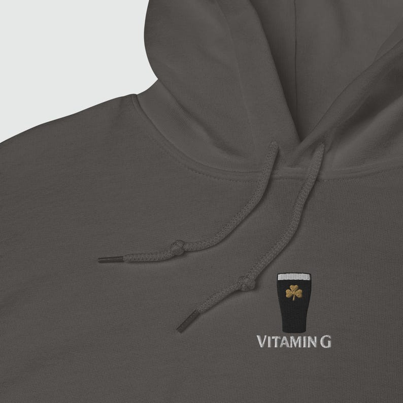 May include: A dark gray hoodie with a drawstring and a hood. The hoodie features an embroidered design of a pint of stout with a gold shamrock and the text "VITAMIN G" in white.
