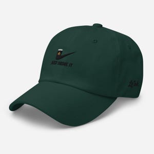 May include: A dark green baseball cap with a curved brim. The cap features an embroidered design of a beer mug with a shamrock and the text "JUST DRINK IT". The brand name "LoInk" is embroidered on the side.