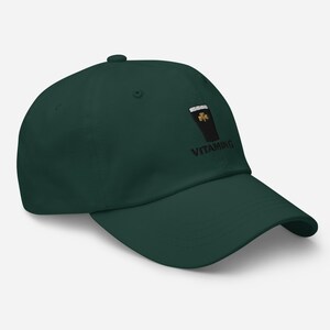 K&ouml;nnte beinhalten: Dunkelgr&uuml;ne Baseballkappe mit einem gestickten Design eines Pints Stout, einem Kleeblatt und dem Wort "VITAMING" in Schwarz. Die Kappe hat einen gebogenen Schirm und einen Knopf oben.