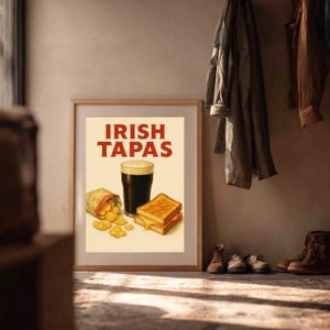 May include: A framed print with the words "IRISH TAPAS" in red. The image features a pint of dark beer, a bag of chips, and two grilled cheese sandwiches. The print is in a room with coats hanging on the wall and shoes on the floor.