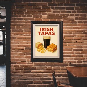 May include: A framed poster with the words "IRISH TAPAS" in red. The poster features a pint of dark beer, a grilled cheese sandwich, and a bag of chips. The poster is hanging on a brick wall.