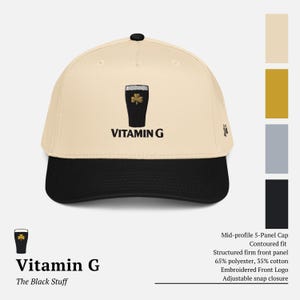 May include: A beige and black baseball cap with the text "VITAMIN G" and a graphic of a black pint of stout with a shamrock. The cap has a structured front panel and an adjustable snap closure.