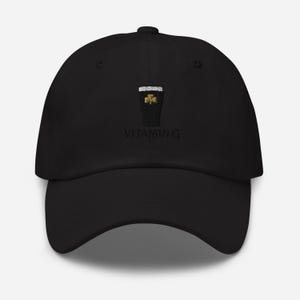 K&ouml;nnte beinhalten: Schwarze Baseballkappe mit gebogenem Schirm. Die Kappe hat ein gesticktes Design eines Pints Stout mit einem Kleeblatt und dem Text "VITAMIN G". Die Kappe ist aus einem weichen Material gefertigt.