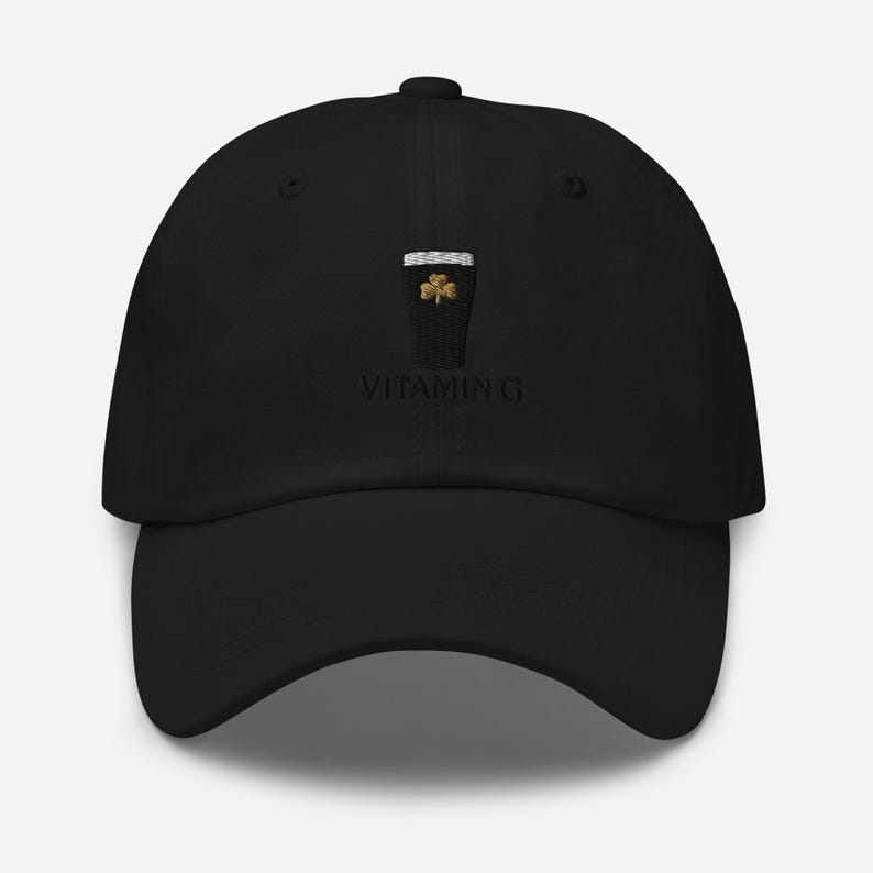 K&ouml;nnte beinhalten: Schwarze Baseballkappe mit gebogenem Schirm. Die Kappe hat ein gesticktes Design eines Pints Stout mit einem Kleeblatt und dem Text "VITAMIN G". Die Kappe ist aus einem weichen Material gefertigt.