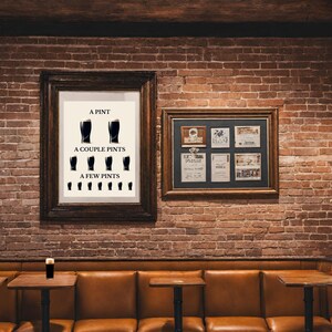 May include: Two framed artworks hang on a brick wall. One features a print with the text "A Pint, A Couple Pints, A Few Pints" and illustrations of beer glasses. The other frame contains several smaller framed items. A pint of beer sits on a small table.