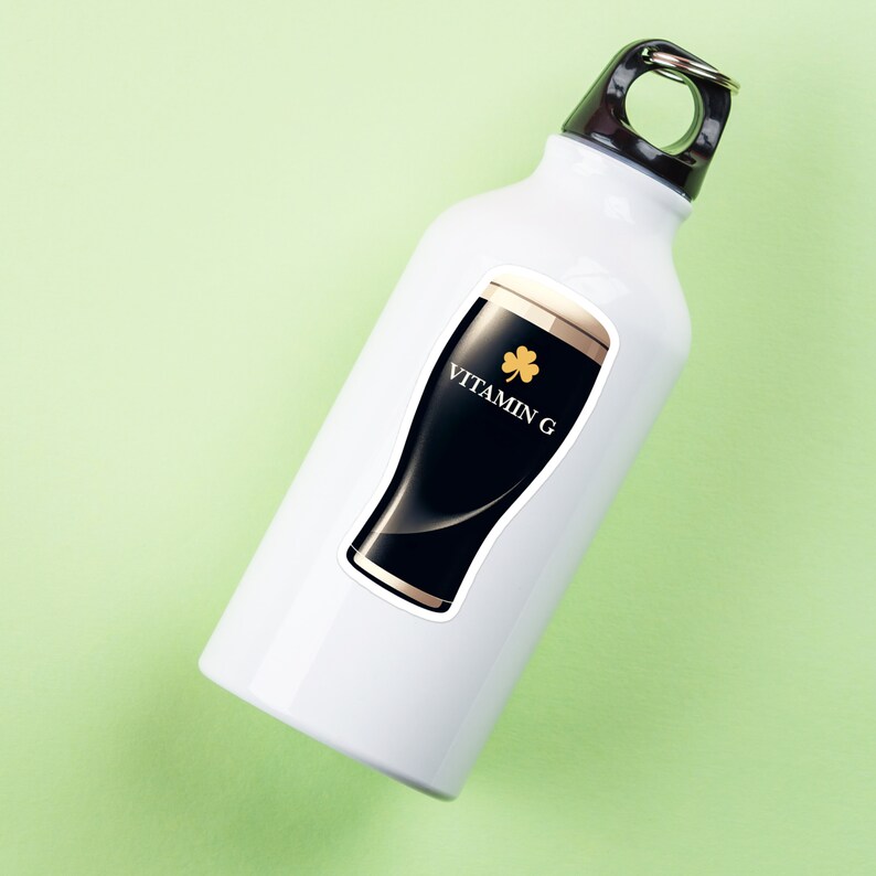 May include: White water bottle with a black and gold graphic of a pint of stout beer. The graphic includes the text "VITAMIN G" and a gold shamrock. The bottle has a silver loop at the top and is set against a light green background.