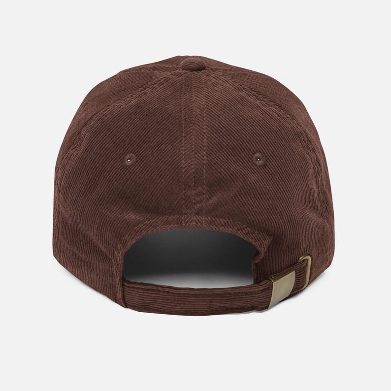 May include: A brown corduroy baseball cap with a curved brim. The back features an adjustable strap with a brass-colored metal buckle. The cap has a classic six-panel design and a button on top.