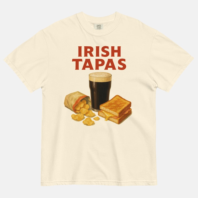 May include: Cream-colored t-shirt with the text "IRISH TAPAS" in red. The graphic features a pint of dark beer, a bag of chips, and a grilled cheese sandwich. The shirt is made of a soft, comfortable material.