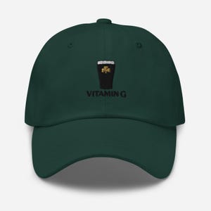 K&ouml;nnte beinhalten: Dunkelgr&uuml;ne Baseballkappe mit gebogenem Schirm. Die Kappe hat ein gesticktes Design eines Pints Stout mit einem Kleeblatt und dem Text "VITAMIN G" in Schwarz.