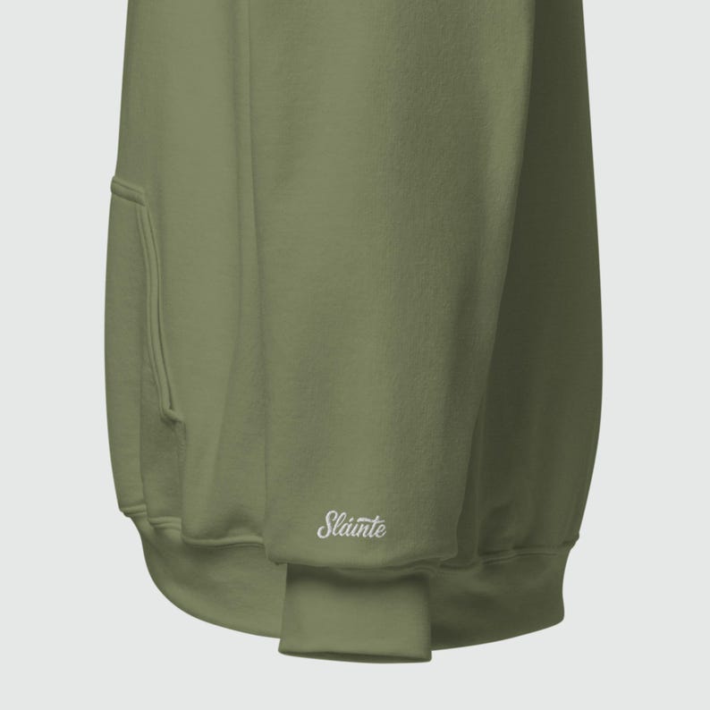 May include: Olive green hoodie with a kangaroo pocket and ribbed cuffs. The word "Sl&aacute;inte" is embroidered in white on the cuff. The hoodie is made of a soft, comfortable material.