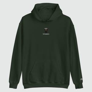 May include: Dark green hoodie with a front pocket and a hood. The hoodie features a small embroidered design of a coffee cup with a shamrock and the text "VITAMIN G". The sleeve has a small embroidered "St" logo.