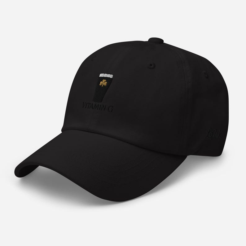 K&ouml;nnte beinhalten: Schwarze Baseballkappe mit gebogenem Schirm. Die Kappe hat ein gesticktes Design eines Pints Stout mit einem Kleeblatt und dem Text "VITAMIN G". Ein klassisches, l&auml;ssiges Accessoire.