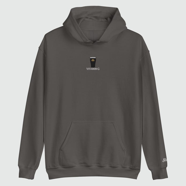 May include: A dark gray hoodie with a front pocket and a hood. The hoodie features a small graphic of a pint of stout with a shamrock and the text "VITAMIN G" printed below. The sleeve has a small embroidered logo.