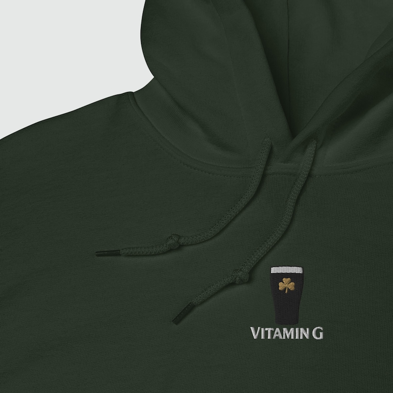 May include: Dark green hoodie with a drawstring hood. The hoodie features an embroidered design of a black pint glass with a gold shamrock and the text "VITAMIN G" in white.