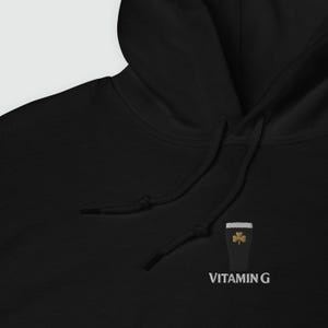 May include: Black hoodie with a drawstring and a small embroidered design of a pint of stout with a gold shamrock. The text "VITAMIN G" is embroidered below the design.