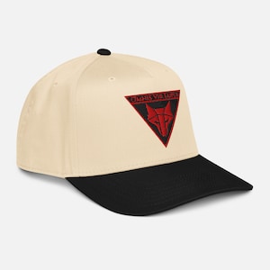 Puede incluir: Gorra de béisbol color crema con visera negra. La gorra presenta un triángulo rojo bordado con un diseño de cabeza de lobo y el texto "OMNIS VIA LUPUS". La gorra tiene una visera curva y un botón en la parte superior.