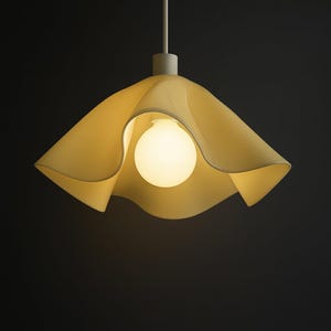 May include: A contemporary pendant light featuring a pale yellow, petal-like shade. A spherical light bulb is encased within the shade. The light hangs from a white rod against a dark backdrop.