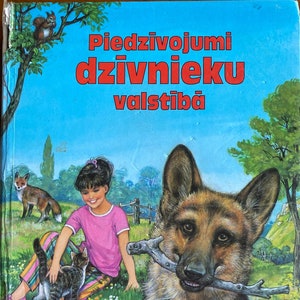 May include: A book cover with a colorful illustration of a girl, a dog, a cat, and a magpie. The title of the book is "Piedzivojumu dzivnieku valstiba" and the publisher is "Sprīdītis".