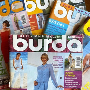Könnte beinhalten: Ein Stapel bunter Magazine mit dem Titel "Burda" und dem Text "Весь мир моды" (bedeutet "Die ganze Welt der Mode") in Russisch. Die Magazine zeigen Modeentwürfe und Artikel.