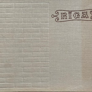 May include: A vintage book cover with a textured, light gray fabric background. The left side of the cover has a brick pattern. The right side of the cover has the word "RIGA" in a decorative font.