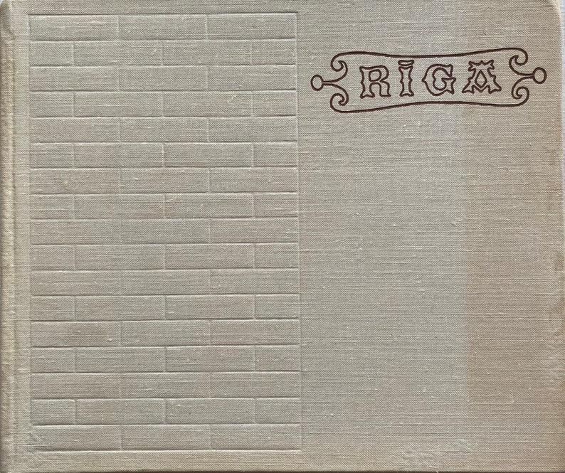 May include: A vintage book cover with a textured, light gray fabric background. The left side of the cover has a brick pattern. The right side of the cover has the word "RIGA" in a decorative font.