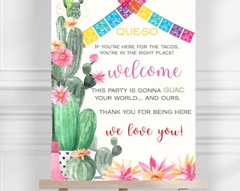 May include: A white welcome sign on an easel with the text "QUE-SO" and "welcome". The sign features watercolor illustrations of cacti, pink flowers, and colorful papel picado banners. The sign reads "If you're here for the tacos, you're in the right place!"