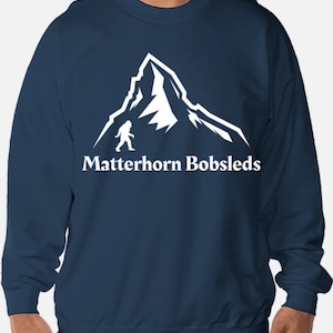 May include: A navy blue sweatshirt with a white graphic of a mountain and a figure walking on it. The text "Matterhorn Bobsleds" is below the graphic.