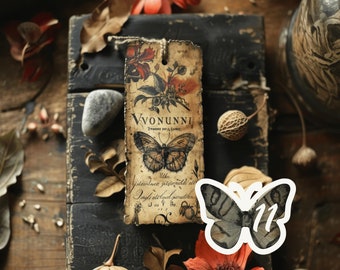 May include: A vintage style bookmark with a floral design and a butterfly illustration. The bookmark is made of paper and has a brown and cream color scheme. The text on the bookmark reads "Vvonunni".