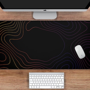 May include: A black desk mat with a topographic design in shades of orange, purple, and yellow. The mat is rectangular, measuring 31 inches by 15.5 inches, and features a white mouse and keyboard. A computer monitor is visible above.