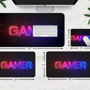 May include: A set of four gaming mouse pads with a black background and neon pink, blue, and purple text. The largest mouse pad is 31 inches by 15.5 inches and features the word "GAMER". The other three mouse pads are 18 inches by 12 inches, 22 inches by 12 inches, and 9 inches by 7 inches, and feature the word "GAMER" in different styles.