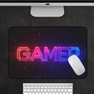 May include: A black mouse pad with a neon pink and blue "GAMER" graphic on a black background with a white mouse on the pad.