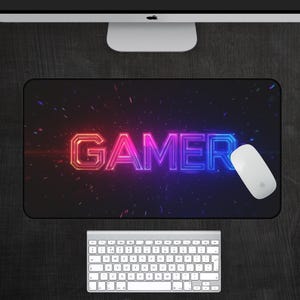 May include: A black gaming mouse pad with a neon pink and blue "GAMER" text graphic. The background has a subtle sparkle effect.