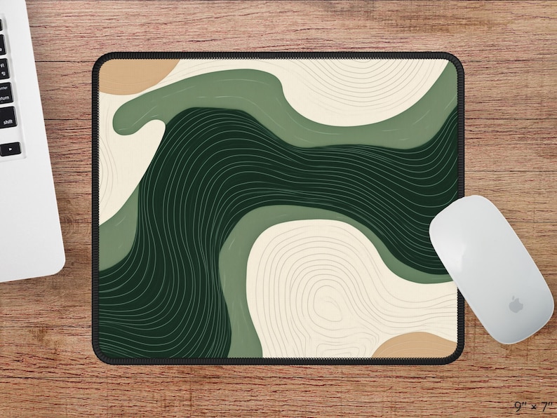 May include: Rectangular mouse mat with a black border, featuring an abstract design in shades of green, beige, and dark green. The design includes curved lines and shapes. A white mouse is next to the mat. The mat measures 22.86cm x 17.78cm.