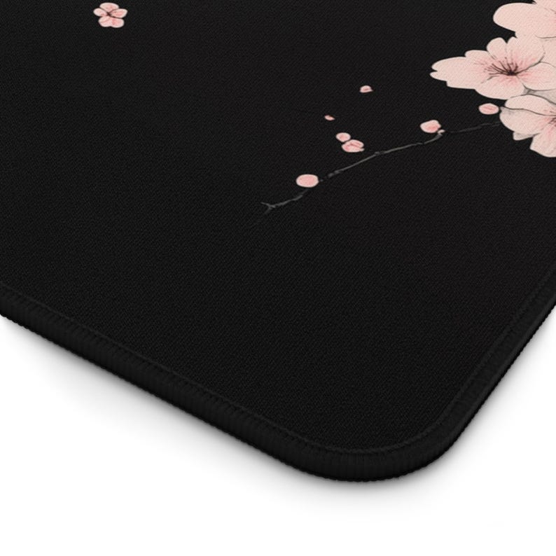 Puede incluir: Alfombrilla de rat&oacute;n negra con un delicado dise&ntilde;o de flores de cerezo rosas en una rama. El dise&ntilde;o es sutil y elegante, a&ntilde;adiendo un toque de naturaleza a tu espacio de trabajo.
