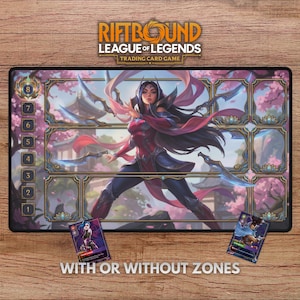 May include: A rectangular playmat for the Riftbound League of Legends trading card game featuring a central illustration of a female character with long dark hair, surrounded by game zones, numbered slots, and two small game cards.