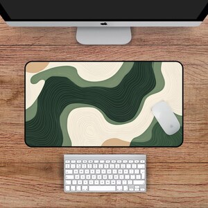 May include: A rectangular desk mat with a black border, featuring an abstract design in shades of green, beige, and brown. A white computer mouse rests on the mat. The mat measures 56 cm by 30 cm.