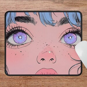 Op de afbeelding: Een muismat met een close-up van een vrouwengezicht met grote, paarse ogen en roze huid. De vrouw heeft blauw haar en is getekend in een cartoon stijl.