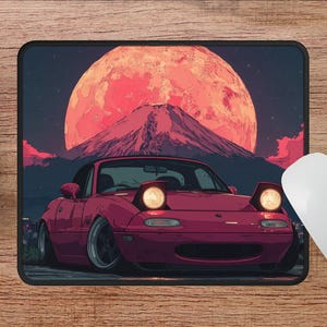 Puede incluir: Alfombrilla de rat&oacute;n con un coche deportivo granate con faros emergentes, sobre un fondo de un gran sol rojo y una monta&ntilde;a. La alfombrilla es rectangular, con dimensiones de 22,86 cm x 17,78 cm.