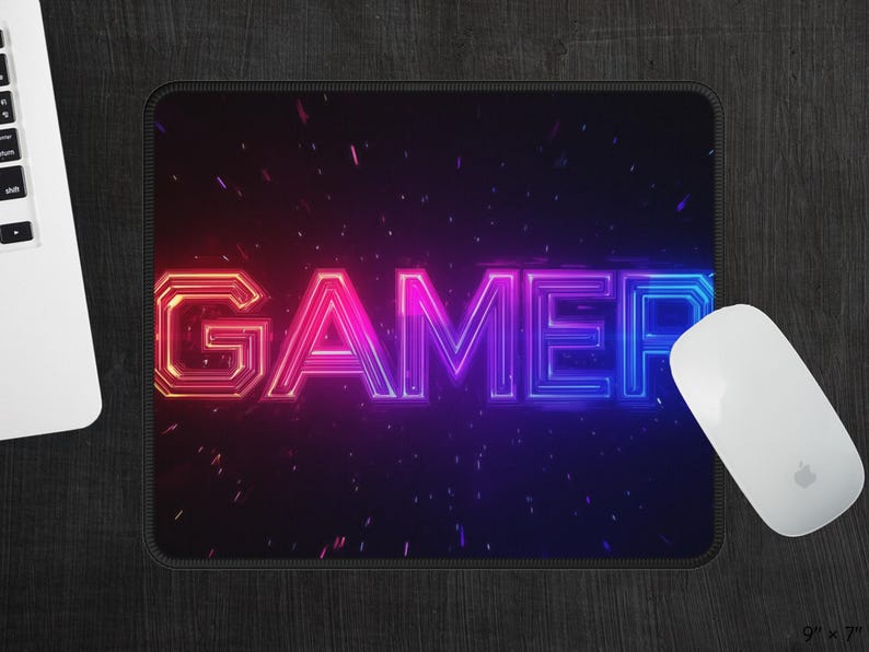 May include: A black mouse pad with the word "GAMER" in neon pink and blue lettering. The letters are outlined in white and have a pixelated effect. The background is black with a subtle sparkle effect.