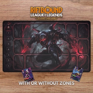 May include: A black Riftbound League of Legends trading card game playmat with a dark illustration of a character and red accents. The mat has numbered zones and the text "WITH OR WITHOUT ZONES". Two trading cards are placed on the wooden surface.