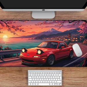 May include: A red sports car mouse mat featuring a Japanese landscape with a mountain, cherry blossoms, and a sunset. The mat measures 78.7 cm by 39.4 cm, with a winding road and a white computer mouse.