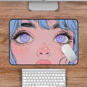 Op de afbeelding: Een anime-stijl illustratie van een vrouwen gezicht met paarse ogen, in blauw en roze. De illustratie is op een muismat.