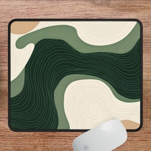 May include: Rectangular mouse mat with a black border. It features an abstract design of flowing shapes in green, beige, and dark green, with thin, curved lines. A white computer mouse and keyboard are visible.