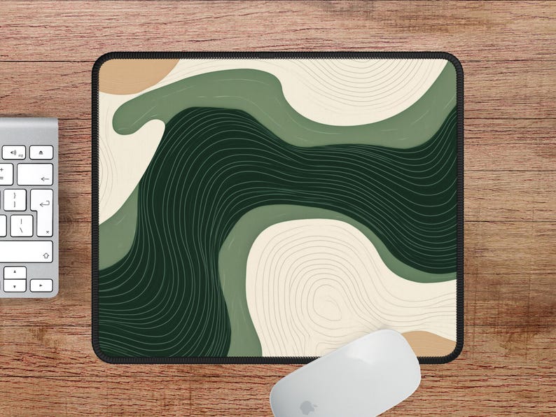 May include: Rectangular mouse mat with a black border. It features an abstract design of flowing shapes in green, beige, and dark green, with thin, curved lines. A white computer mouse and keyboard are visible.