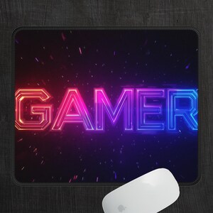 May include: A black mouse pad with a neon pink and blue "GAMER" graphic. The graphic is surrounded by a dark blue background with white speckles.