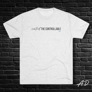 May include: A heather grey t-shirt with the text "control THE CONTROLLABLE" printed in black on the front. The text is in a handwritten font.