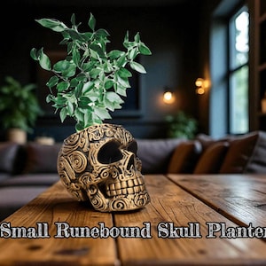 May include: A gold-colored skull-shaped planter with intricate patterns, holding a vibrant green plant. The planter sits on a wooden table. Text at the bottom reads "Small Runebound Skull Planter".