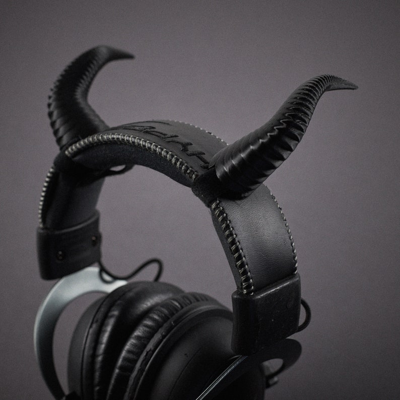 May include: Black headphones with a stitched leather headband and two black horns on top.