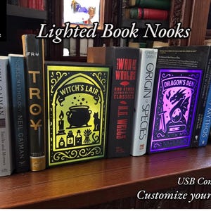 May include: Illuminated book nooks with designs like "Witch's Lair" and "Dragon's Den" are displayed. The books are lit with bright colours and have USB connections. The text "Customize your own!" is also visible.