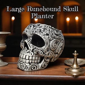 May include: A large, silver-colored skull planter with intricate runic designs. The skull has a detailed, textured surface and is set on a wooden table. The text "Large Runebound Skull Planter" is at the top of the image. Other decorative items are also on the table.
